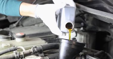 Eldivendeki tamirci elleri motor yağını araba motoruna döker. İşçi bakım sırasında şişeyi eğip rezervuar kontrol seviyesini doldurur