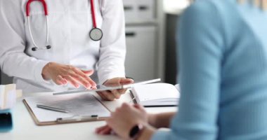 Kadın doktor ekranı işaret eden tablet üzerinde tedavi planı gösteriyor. Hasta kadın, randevuda seçenekleri değerlendirir ve sorular sorar.