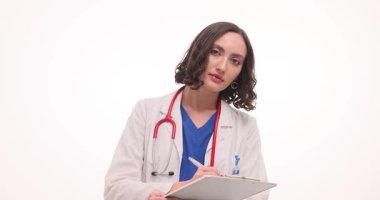 Güneşli bir klinik odasında, beyaz önlüklü odaklanmış bir doktor hasta detaylarını not alıyor. Kapsamlı bir muayeneye hazırlanırken şefkat ve profesyonellik gösteriyor..