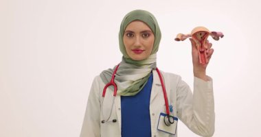 Jinekolog, beyaz arka planda rahmin ve hijyenik pedin anatomik modelini tutuyor. Müslüman doktor adet görme sürecini açıklıyor. Yavaş çekim
