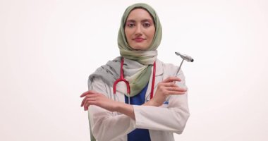 Tesettürlü mutlu kadın doktor refleks çekici tutuyor ve beyaz arka planda kollarını kavuşturuyor. Müslüman doktorlar kameraya poz veriyor. Yavaş çekim