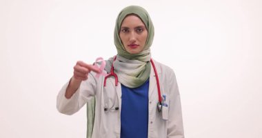 Tesettürlü kadın doktor beyaz arka planda pembe kurdele tutuyor. Müslüman doktor meme kanseri farkındalığının önemini vurguladı. Yavaş çekim