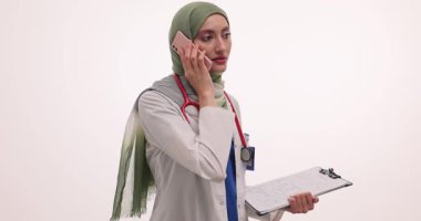 Türbanlı doktor beyaz arka plandaki hastaya test sonuçlarını açıklıyor. Müslüman kadın hastaya ağır çekimde tıbbi durumdan bahsediyor