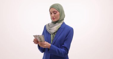 Tesettürlü iş kadını beyaz arka plandaki banknotları dikkatle sayıyor. Müslüman kadın nakit rüşvet miktarını doğruladı. Yavaş çekim