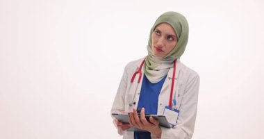 Kadın doktor teşhisi düşünürken pano tutuyor. Türbanlı Müslüman doktor, sakin odaklı ağır çekimde tedavi adımları planladığına dikkat çekti