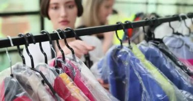 Askıda plastik kaplı giysiler, beyaz tenli personel giysileri kuru temizleme takımları, elbise elleri, düzenli koruma sıraları.