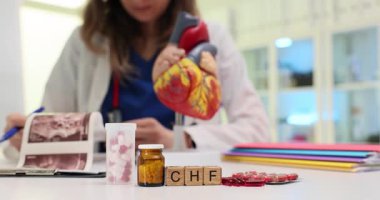 Tahta bloklar kalp modeline yakın CHF sözcüğünü hecelerken, kadın kardiyolog hasta kayıtlarını inceliyor. Kadın doktor CHF sorununu açıklayan kalp modelini inceliyor