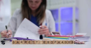 Terim Barrett Esophagus, klinik masasındaki tahta bloklarda hapların yanında görünüyor. Kadın gastroenterolog hasta reflüsü planının düzeltildiğini okudu