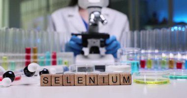 Tahta küplerin Selenyum 'unu cam eşyalar arasında kimyagerin işyerindeki renk sıvılarıyla birlikte yaz. Mikroskop kullanan kadın bilim adamı laboratuvarda mineralleri analiz ediyor.