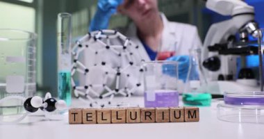 Ahşap bloklardan ve moleküler modelden oluşan kelime Tellurium 'u eczane masasındaki renk sıvılarına göre. Kadın bilim adamı tıp laboratuarında son derece nadir bulunan bir metalle çalışıyor.