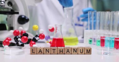 Tahta blokların Lanthanum 'unu renk sıvılarıyla ve kimyasal laboratuardaki moleküler modellerle yaz. Kadın araştırmacı iş yerinde nadir bulunan metallerle testler yapıyor.