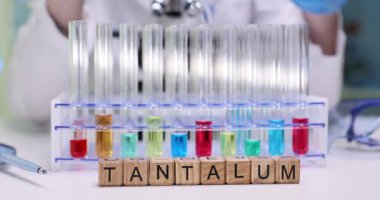 Tahta bloklardan ve kimyagerin ellerinden oluşan kelime Tantalum test tüplerini laboratuardaki renk sıvılarıyla yeniden düzenliyor. Kimyasal reaksiyonlu nadir metalleri araştırıyorum.