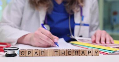 Kadın doktor ultrason görüntülerini inceler ve gözlemlerini yazar. Masanın üzerindeki minyatür tahta küpler açıkça masada 