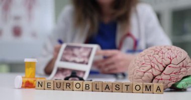 Tahta bloklar, anatomik beyin modelinin yanındaki masada nöroblastoma kelimelerini oluşturur. Kadın doktor, hastanın ultrason görüntülerini inceliyor.
