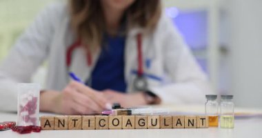 Tahta bloklar parlayan steril tıp masasında antikoagülan kelimesini haplarla hecelerler. Kadın doktor klinikte kan testi için şırınga hazırlıyor.