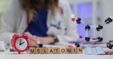 Tahta bloklar Melatonin sözcüğünü kırmızı alarm saatine yakın gösteriyor. Kadın doktor, mavi tabletli molekül modelleme paketi üzerinde çalışıyor.