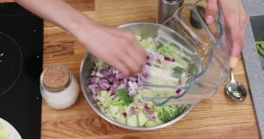 Ellerin ahşap masada metal kasede sebze salatasını karıştırıyor. Aşçı lahanaya baharat katar ve soğan ilave eder. Malzemeleri kaşıkla karıştırır, öğle yemeği pişirir.