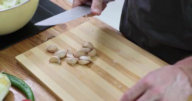 Ahşap kesme tahtasına sarımsak kabuğu soyarak yemek pişirmek. Taze sebzeler yakınlarda yatarken, insan yemek için baharatlı malzemeler hazırlıyor.