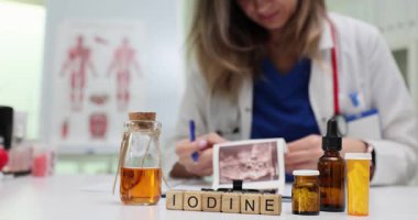 Ahşap blok sırası kahverengi ilaç şişelerinin yanında iyot anlamına gelir. Kadın doktor, antiseptik kullanım tavsiyesine dikkat çeken ultrason görüntüsü çıktısı üzerinde çalışıyor