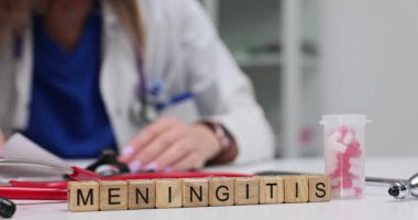 Tahta bloklar ilaç ve şişelerin yanında menenjit olduğunu gösteriyor. Beyaz önlüklü kadın doktor randevuda hasta tedavi planını kontrol eden notlar yazar.