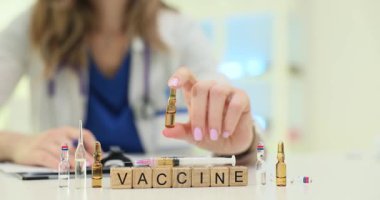 Temiz beyaz önlüklü kadın doktor küçük şeffaf ampul ve ilaç gösteriyor. Masanın üzerinde minyatür tahta küpler var.