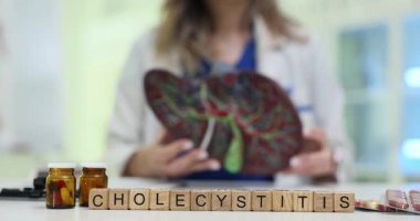 Tahta küpleri düzgün bir şekilde masa biçiminde kolesistit kelimesine yerleştirilmiş. Kadın doktor, öğrencilere karaciğer yapısını açıklayan anatomik modelini tutuyor.