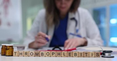 Masanın üzerinde minyatür tahta küpler Thrombophlebitis kelimesi var. Kadın doktor hasta tedavi formunda tıbbi talimatlar yazıyor.