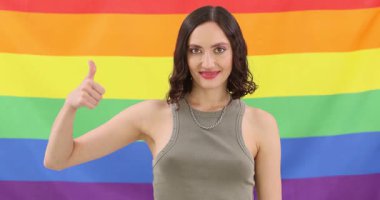 Gülümseyen kadın gökkuşağı gurur bayrağına karşı duruyor ve baş parmak işareti yapıyor. Destekçi kişi, hoşgörülü tavrını takınırken eşitlik mesajını kutluyor