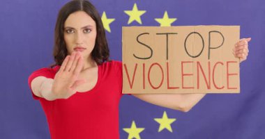 Kırmızı gömlekli kadın, elinde karton levha taşıyan AB bayrağına karşı duruyor: Şiddeti Durdurun. Kadın eylemci, güçlü protesto mesajı göndererek elini kaldırdı