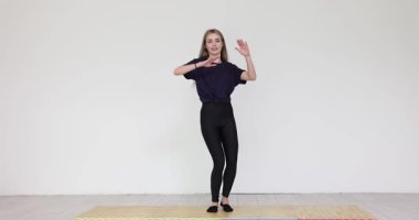 Koyu renk elbiseli genç bir kadın ileriye bakarken halının üzerinde duruyor. Enerjik dişi, yumuşak koluyla dans eder. Yavaş çekimde yavaşça hareket eder.