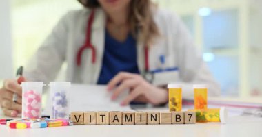 Tahta bloklar tıbbi masanın üzerinde B-7 vitamini yazıyor. Kadın doktor notlar yazıyor, etrafa saçılmış parlak ilave haplarla şişeleri inceliyor.