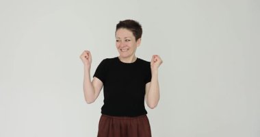 Kısa saçlı neşeli kadın, beyaz arka planda mutluluğu ifade eden yumruklarını sallıyor. Heyecanlı bayan stüdyo yavaş çekimde gol başarısını kutluyor.