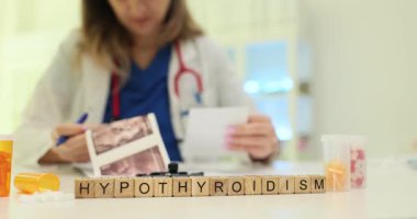 Wooden blocks spell word Hypothyroidism by thyroid scan images. Endocrinology doctor checks report planning therapy for hypothyroidism at appointment