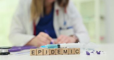 Ahşap bloklar, masanın üzerine şırıngaların yanına salgın kelimesi konur. Enfeksiyon uzmanı aşı yığınını hazırlıyor. Salgın verilerini dikkatlice kaydediyor.