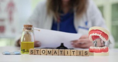 Tahta bloklar Stomatitis kelimesini çene modeli ve gargara şişesiyle heceler. Bayan dişçi hasta mide iltihabı ile ilgili belgeleri randevuda okur