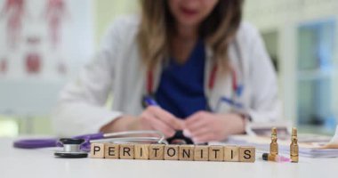 Wooden blocks spell word Peritonitis near stethoscope and ampoules on table. Medical woman writes report prescribing treatment for peritonitis