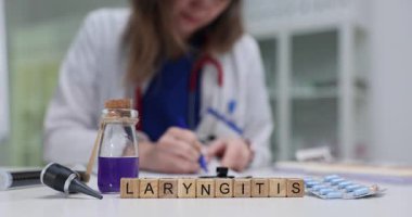 Tahta bloklar, masada mor solüsyon şişesinin yanındaki larenjit kelimesini heceliyorlar. Kadın doktor gırtlak iltihabı tedavisi için planlama notlarını kontrol ediyor.