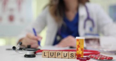 Tahta bloklar steteskop tepsisi ve ilaç şişesinin yanındaki kelime Lupus 'u heceler. Romatoloji doktoru lupus semptomlarının tedaviyle izlendiği notlar yazıyor.