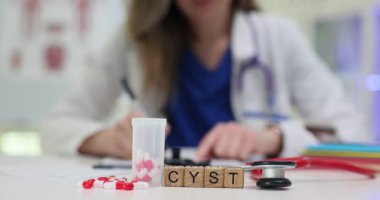 Tahta bloklar kist kelimesini plastik kaplar ve steteskopla hecelerler. Tıp çalışanı, kist teşhisi ve tedaviyi masada tartışan çizelgeyi kontrol ediyor.