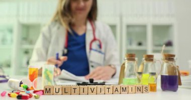 Tahta küplerin yanında renkli haplar ve meyve suyu şişeleri olan multivitaminler var. Kadın doktor diyet takviyelerini gözden geçiren notlar yazar.