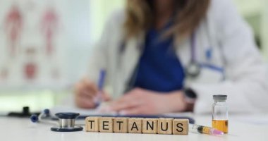 Tahta bloklar, klinikte aşı tehlikesini vurgulayan Tetanos kelimesini heceliyor. Kadın doktor randevudaki hastaya aşı aşısı için not yazar.
