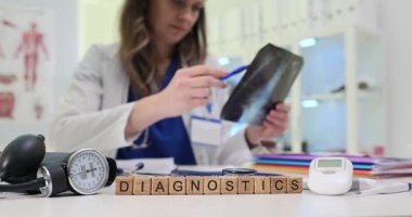 Tahta bloklar basınçlı monitör ve notların yanında kelime tanıları oluşturur. Kadın doktor göğüs röntgeni üzerinde çalışıyor. Klinikteki hastanın risklerini değerlendiriyor.