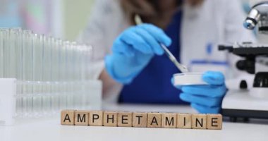 Tahta bloklar test tüpleri ve petri kaplarının yanında amfetamin kelimesini heceler. Kadın bilimadamı, yasadışı uyarıcı madde araştırması için örnek transferi yapıyor.