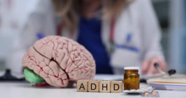 Kadın doktor masada notlar yazarken insan beyni modeli dikkat eksikliği çeken kelimenin yanında duruyor. Uzman, terapiye tepki gösteren dikkat sorunu gözlemliyor