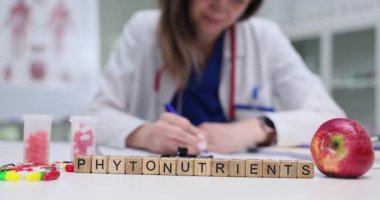 Kadın beslenme uzmanı randevuda kişiselleştirilmiş diyet planı yazıyor. Tahta küpler taze elma ve vitamin şişelerinin yanında Phytonbesin maddeleri oluşturur.