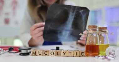 Doktor akciğer alanlarını karşılaştıran radyografik görüntü üzerinde çalışıyor. Tahta bloklar önerilen terapinin bir göstergesi olarak masada Mucolytic dinlenme sözcükleri oluşturur
