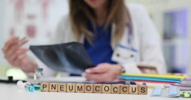 Kadın doktor akciğer radyografisini dikkatle analiz eder. Tahta küp kelime pnömokok oluşturur şüpheli teşhisi göstermek için masada yatar.