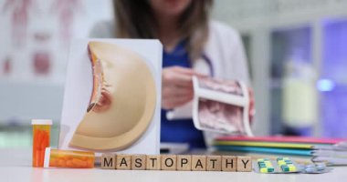 Kadın doktor göğüs ultrasonu ile ilgili detaylı görüntüler üzerinde çalışıyor. Tahta küpler kelime oluşturarak Mastopathy göğüs modeli ve su toplayan ilaç paketlerinin yanında yatar.