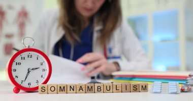 Kadın doktor, uyurgezerlikle ilgili semptomları inceliyor. Ahşap bloklar kurma dönemi uyurgezerliği çalar saatin yanında dinleniyor ve haplar su topladı.