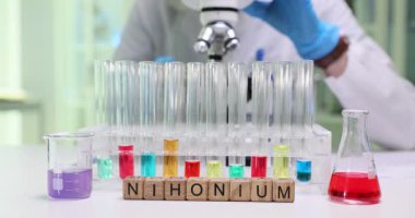 Laboratuvar çalışanı mikroskoba eğiliyor ve cam kaydırağa yerleştirilmiş örnekler üzerinde çalışıyor. Ninonyum terimi soruşturma altındaki maddenin temsili olarak hizmet vermektedir.